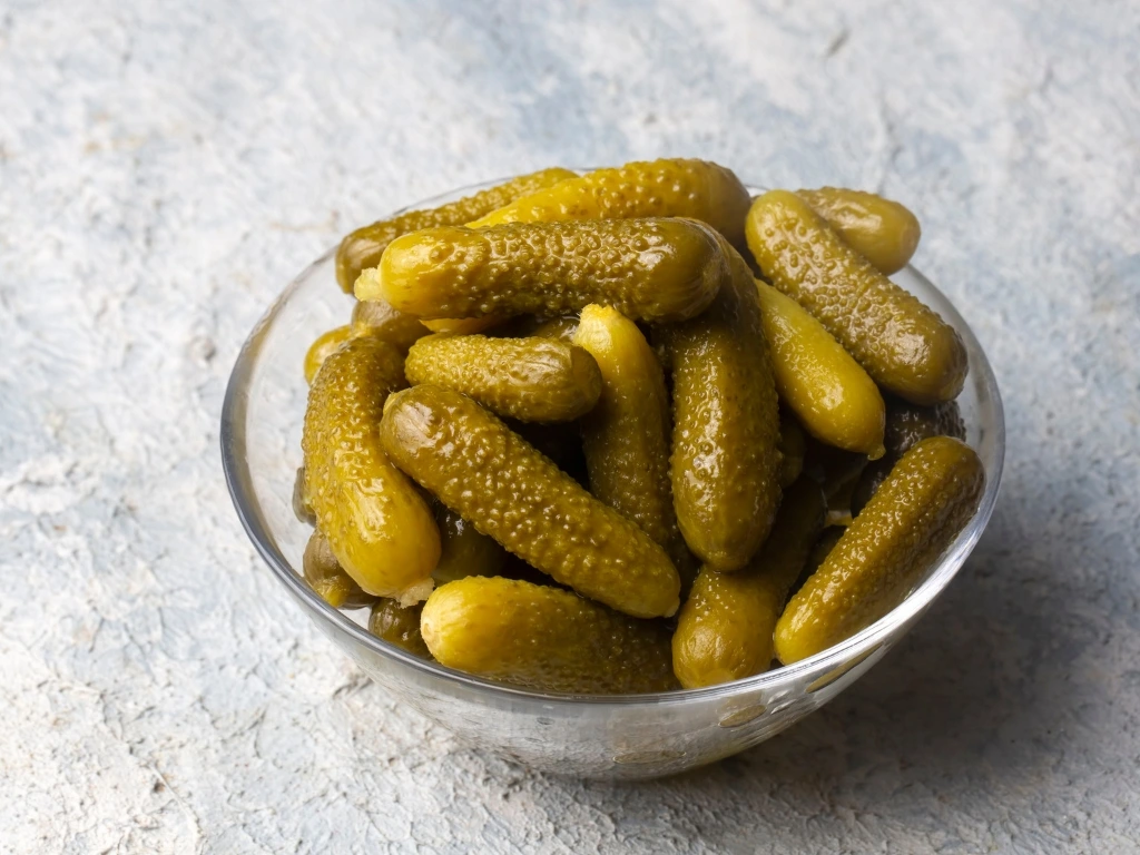 Glass bowl filled with small pickles on a textured light grey surface