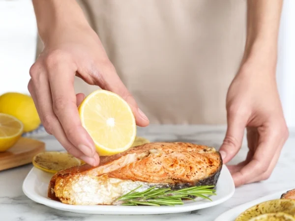 Person preparing a plate of salmon with lemon and rosemary