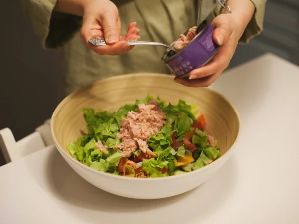 Woman adding canned tuna into a bowl of fresh salad