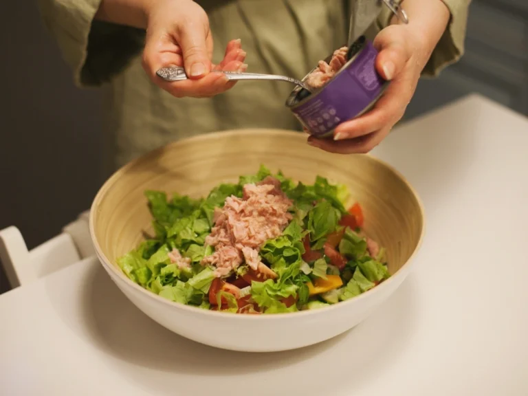 Woman adding canned tuna into a bowl of fresh salad