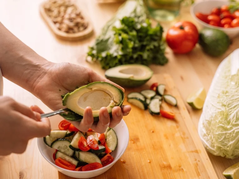 Woman preparing a healthy meal in the kitchen with avocadoes and different vegetables