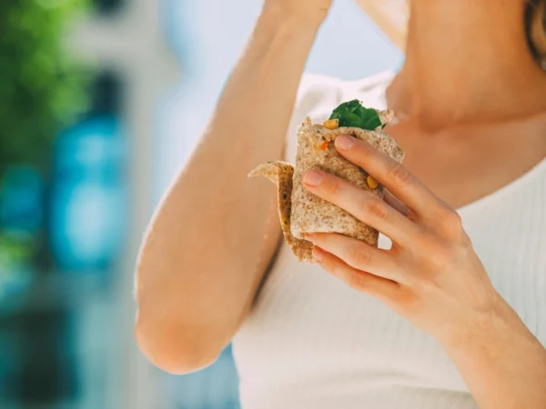 Woman in a white top holding a whole-grain vegetable wrap with fresh greens and corn