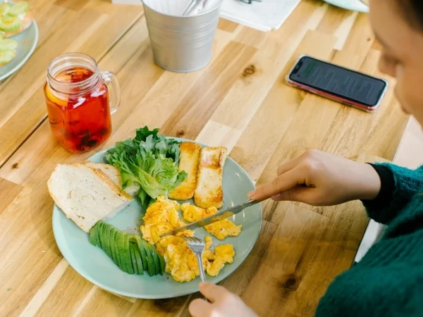 Woman eating scrambled eggs, avocado, bread, and leafy greens