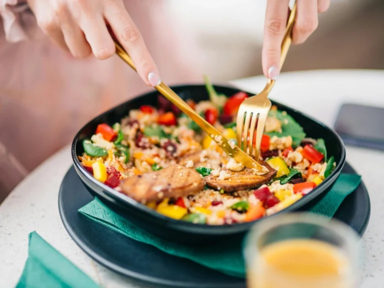 Woman eating a bowl of quinoa salad with fresh, colorful vegetables and seitan strips