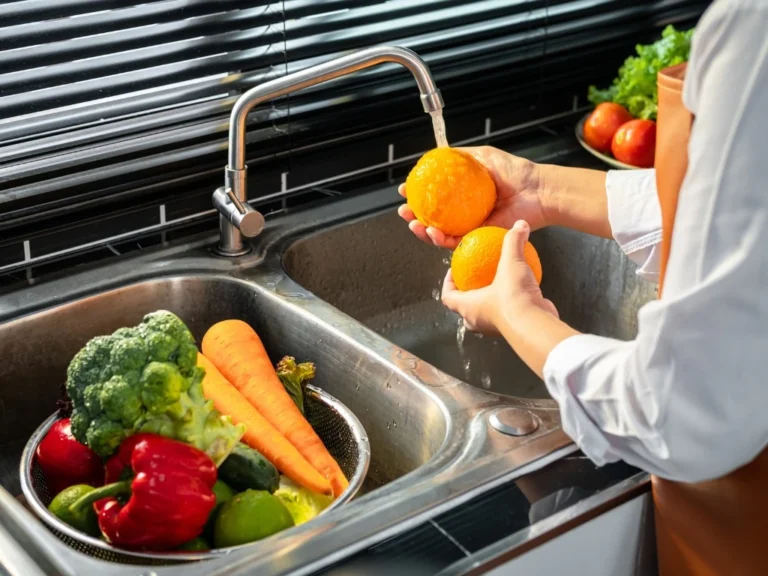 Woman wearing an apron washing produce thoroughly in the kitchen sink