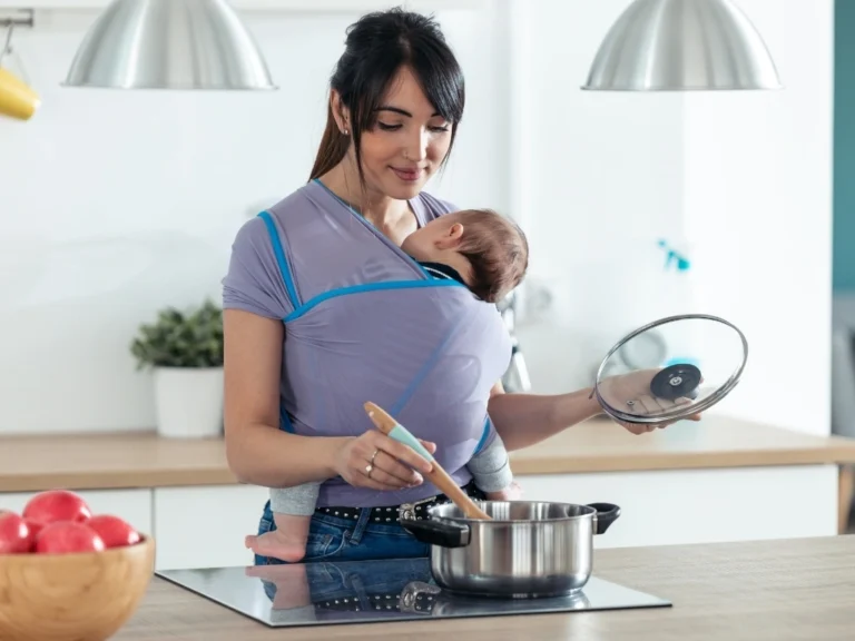 Woman cooking food in the kitchen with a baby in sling