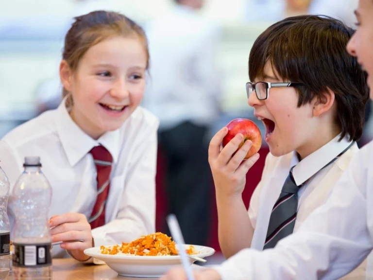 Group of middle schoolers eating and talking in the cafeteria, with a young boy about to bite into an apple
