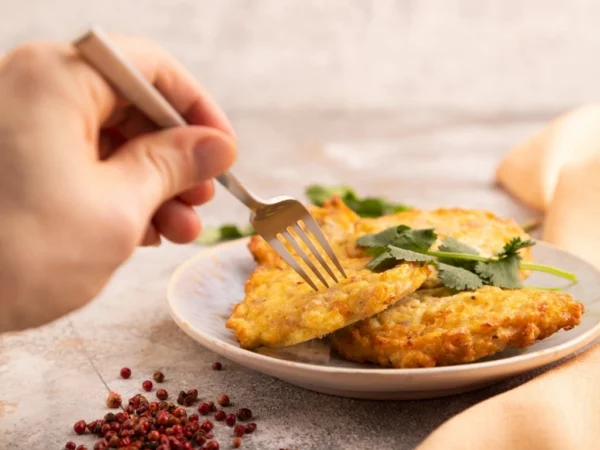 Person getting a piece of a veggie fritter served on a white plate