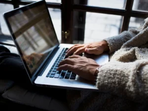 Cropped image of freelancer using laptop while sitting on window sill at cafe