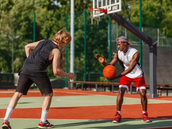 Two sportsmen playing basketball at outdoor arena on summer day