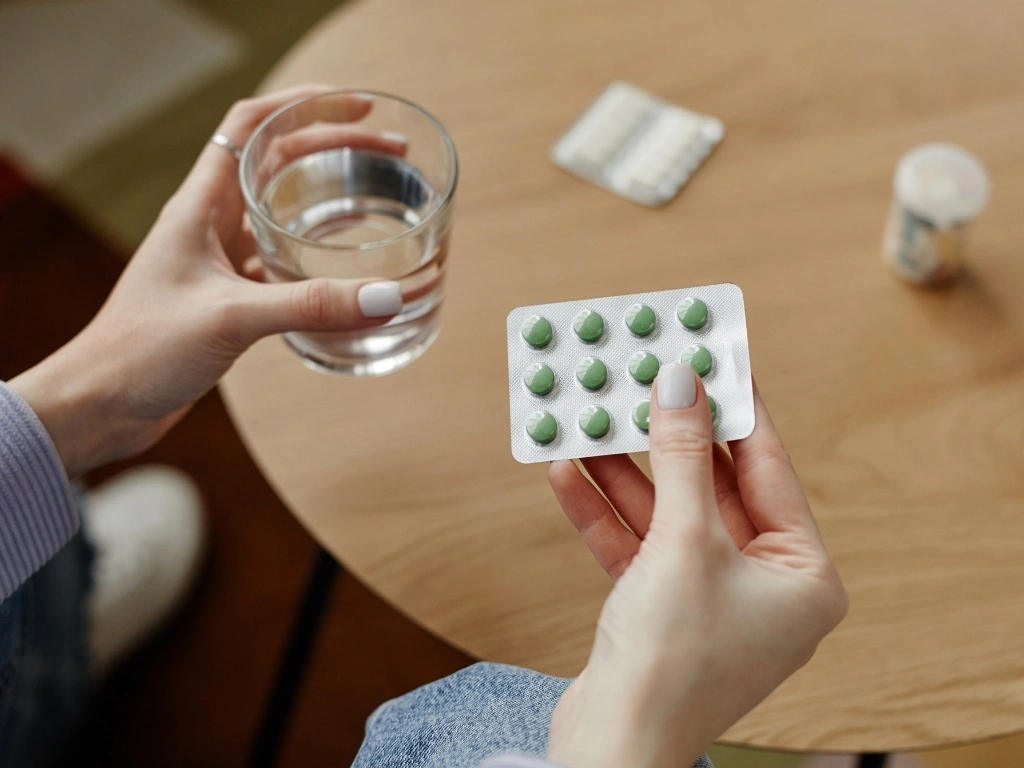 Top view young woman holding pills and glass of water over table