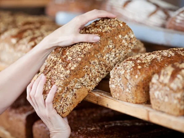 Person taking a seeded bread loaf from a bakery shelf