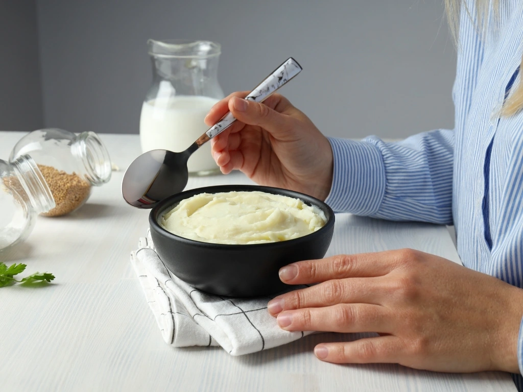 A woman eating a bowl of mashed potatoes with a spoon