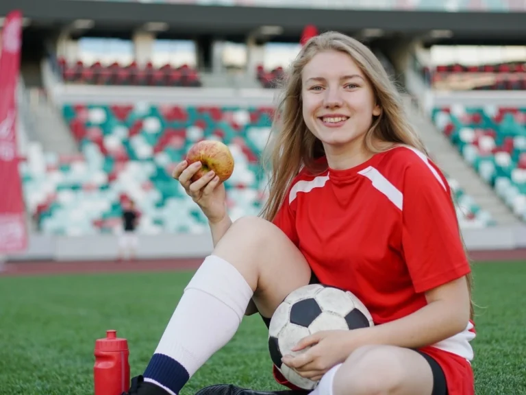 Young soccer player sitting on the field with an apple in hand.