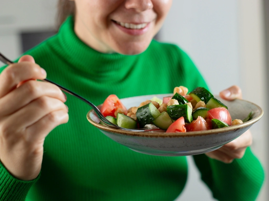 Woman in green eating a cucumber and tomato salad