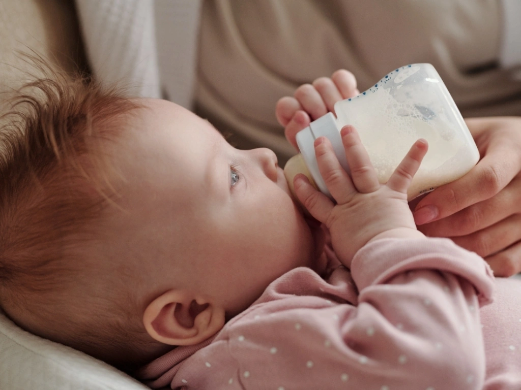 Parent gently holding a bottle to feed a baby with milk