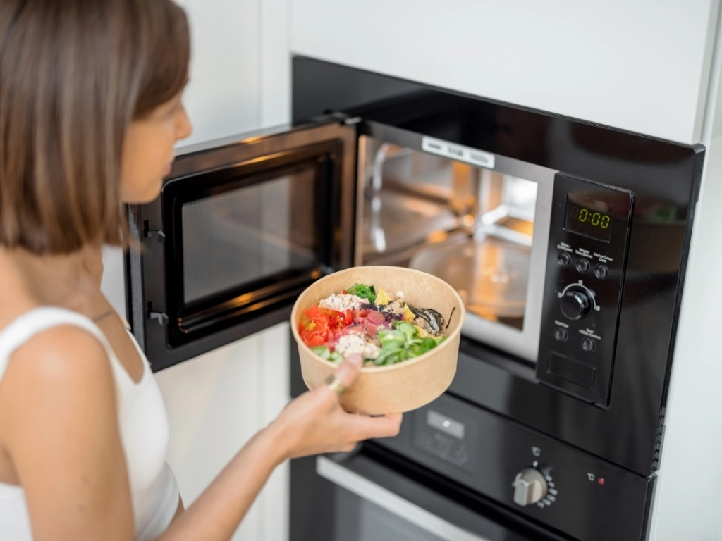 A woman placing a packed meal into an open microwave for heating