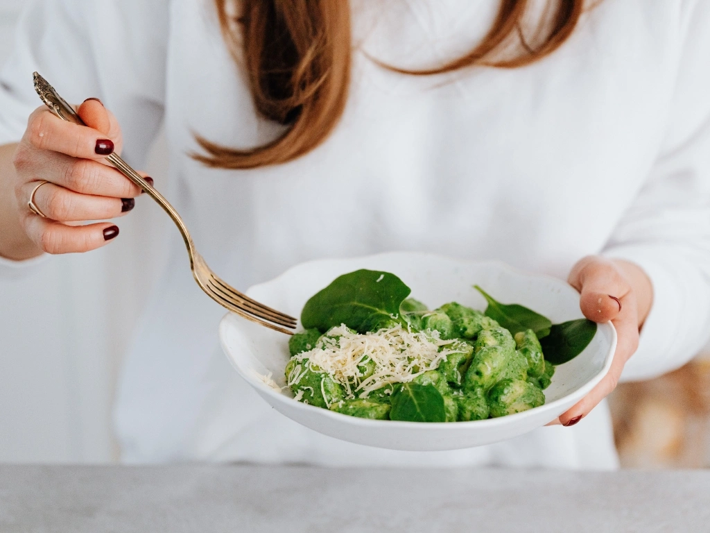Woman in white eating a bowl of low-FODMAP spinach gnocchi with spinach and grated parmesan