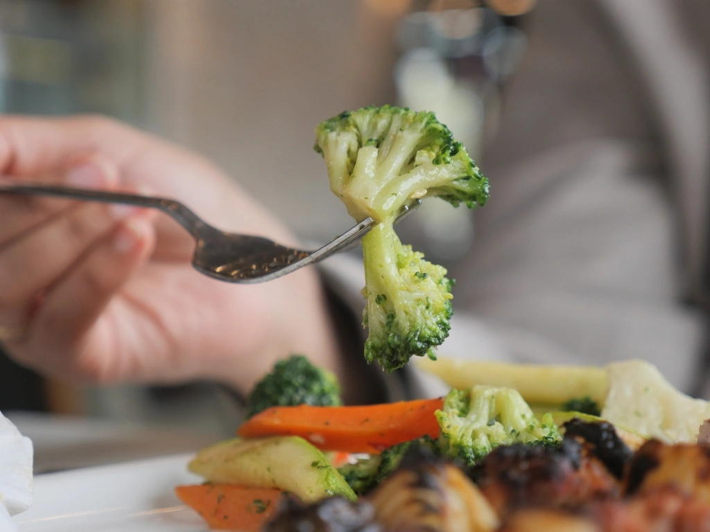 Person picking up a piece of broccoli from a plate full of vegetables using a form