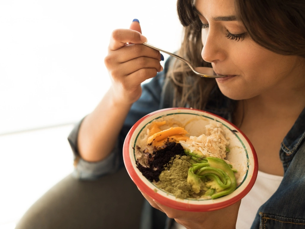 Woman eating a nourishing grain bowl with avocado, rice, vegetables, and greens using a spoon