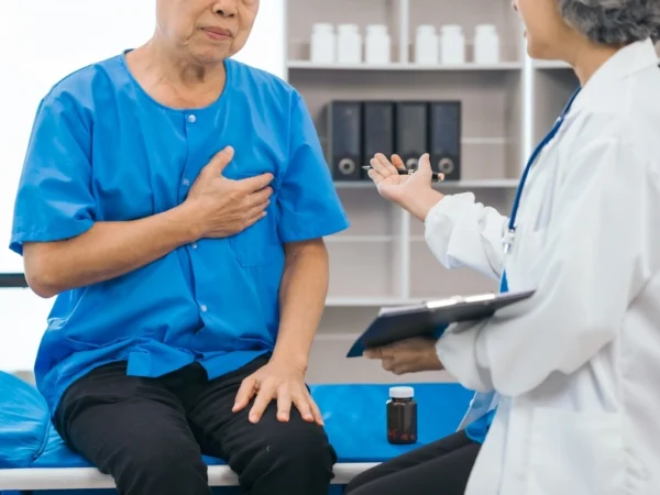 Elderly patient in a blue shirt clutching his chest during a medical checkup with a doctor