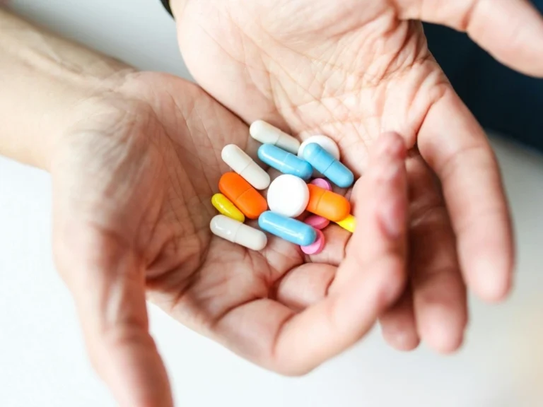 Two cupped hands on a white background, with an assortment of pills in white, orange, yellow, pink, and blue.