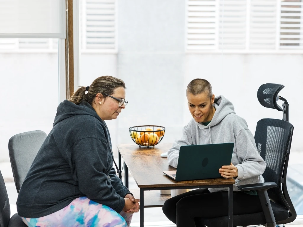 Personal trainer showing workout plan to client on laptop in office
