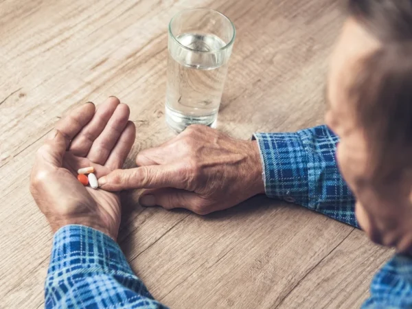 Man seated at a wooden table sorting diabetes medications in his hand, with a glass of water beside him