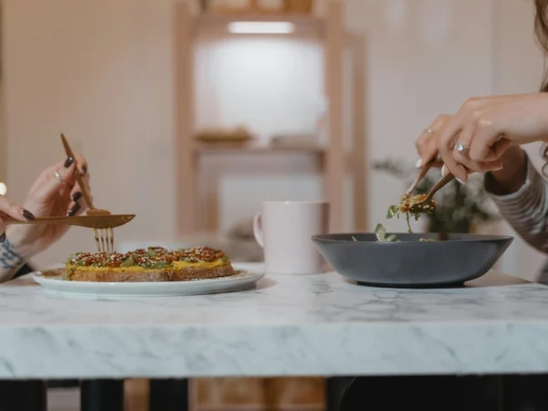 Person Holding Fork and Knife Slicing Food on White Ceramic Plate