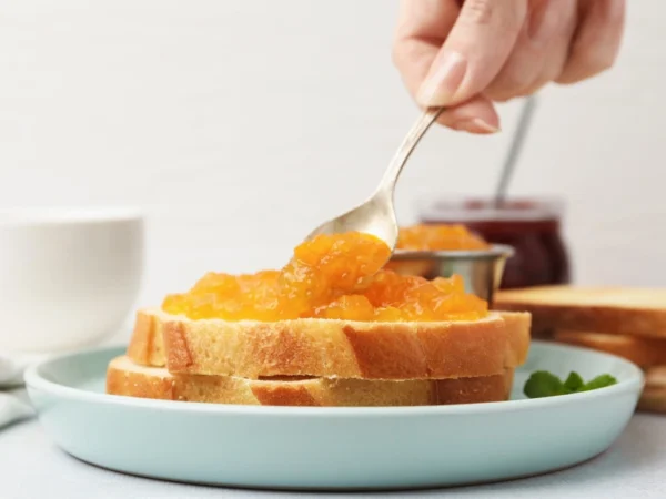 Person spreading apple compote on slices of whole-grain toast stacked on a blue plate
