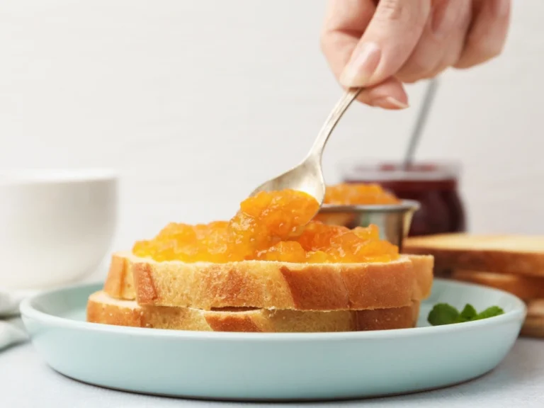 Person spreading apple compote on slices of whole-grain toast stacked on a blue plate
