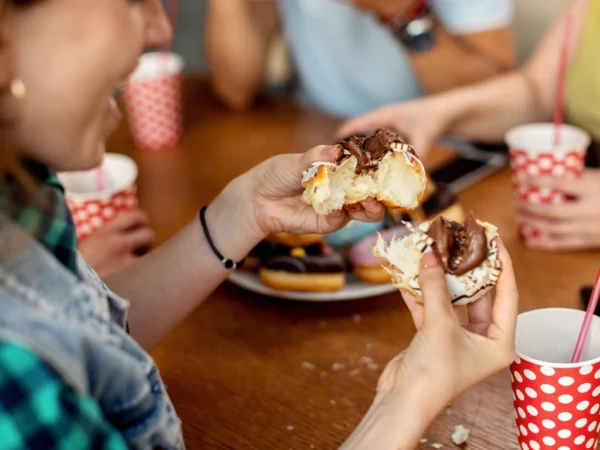 Woman pulling apart a chocolate-filled doughnut at a wooden table with drinks