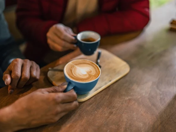 Two people sharing blue cups of coffee with latte art at a wooden table