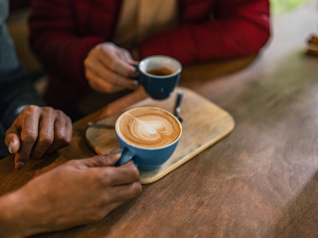 Two people sharing blue cups of coffee with latte art at a wooden table
