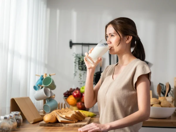 Woman with brown hair drinking a glass of milk in the kitchen