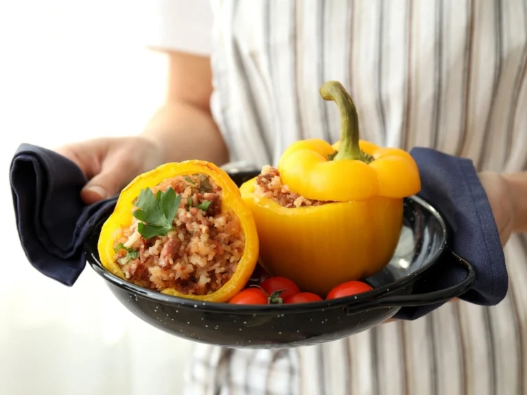 Person serving stuffed yellow peppers and cherry tomatoes on a black plate