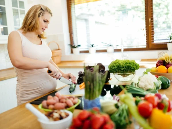A pregnant woman preparing a healthy meal with a variety of colorful vegetables in the kitchen
