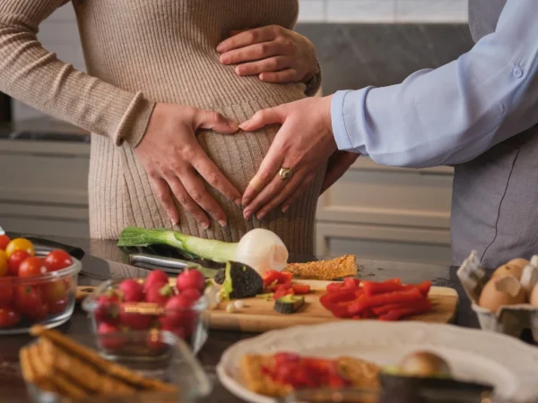 Pregnant couple standing in the kitchen with healthy foods for a balanced diet