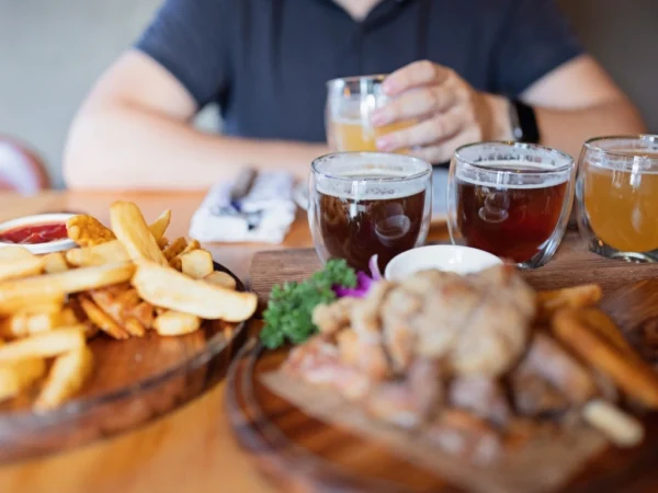 Man seated at a table with different kinds of alcohol, fries, and grilled meat served, holding a glass of beer