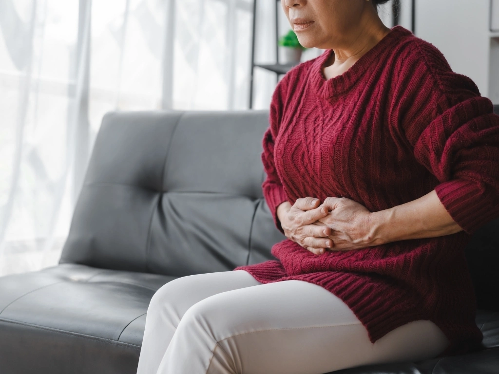 Woman sitting on a sofa, holding her stomach in pain