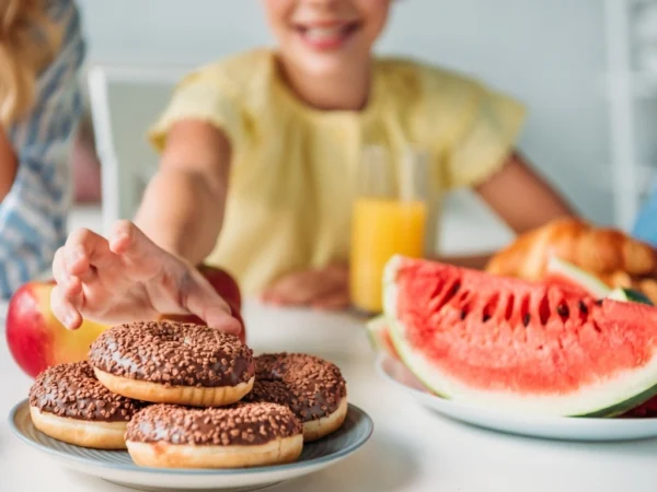 A child reaching for a plate of chocolate donuts next to watermelons