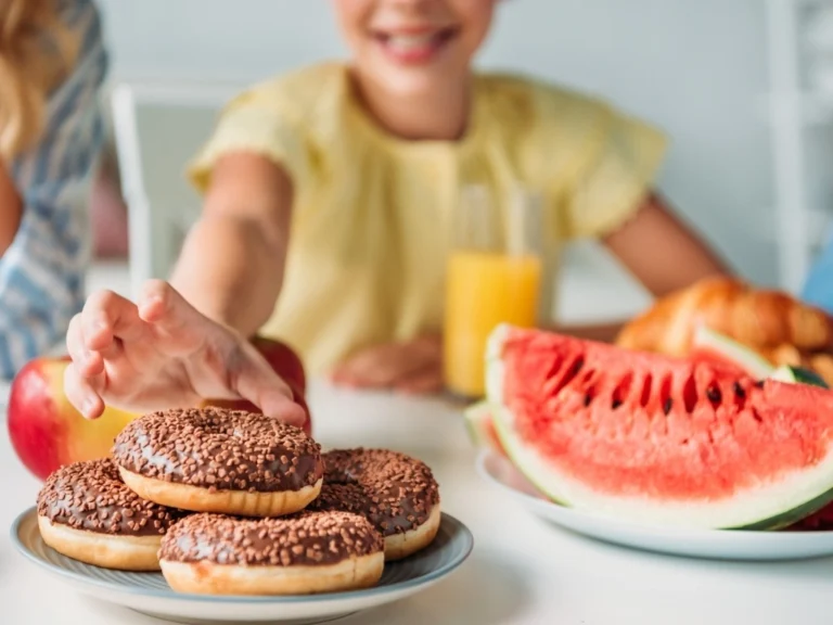 A child reaching for a plate of chocolate donuts next to watermelons