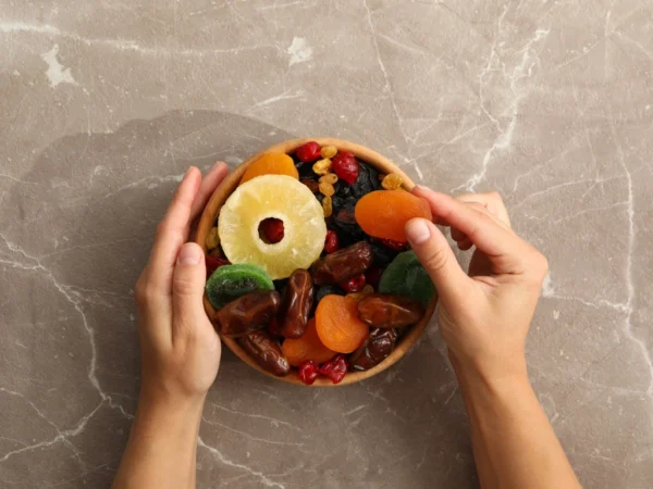 Wooden bowl of assorted dried fruits with hands holding the rim and picking a dried apricot