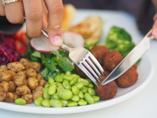 Person using a fork and knife to eat a vegetarian bowl with falafel and chickpeasPerson using a fork and knife to eat a vegetarian bowl with falafel and chickpeas