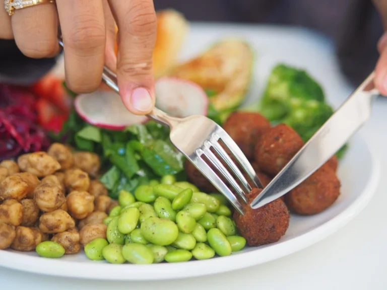 Person using a fork and knife to eat a vegetarian bowl with falafel and chickpeasPerson using a fork and knife to eat a vegetarian bowl with falafel and chickpeas