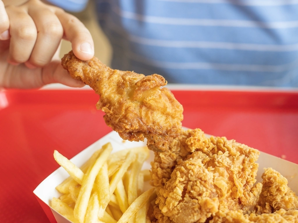 Person getting a piece of fried chicken from a set meal served with French fries
