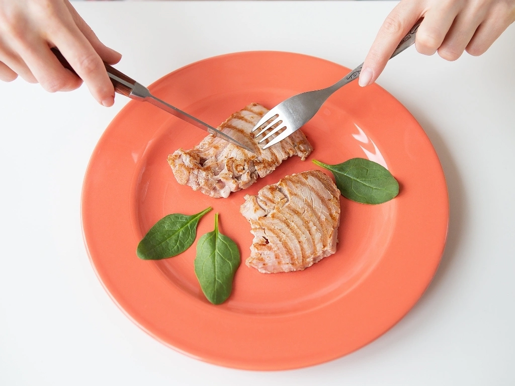A person slicing some grilled tuna steak on a bright coral plate