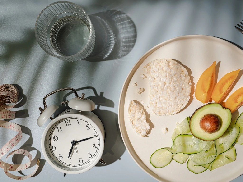 Plate of healthy vegetables and rice cakes alongside an alarm clock and measuring tape