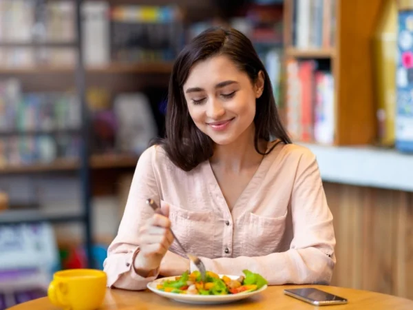 Pretty latin lady tasting fresh healthy salad, sitting at cafe or restaurant in daytime