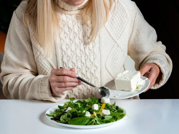 Woman adding cubes of soft cheese to a plate of spinach salad